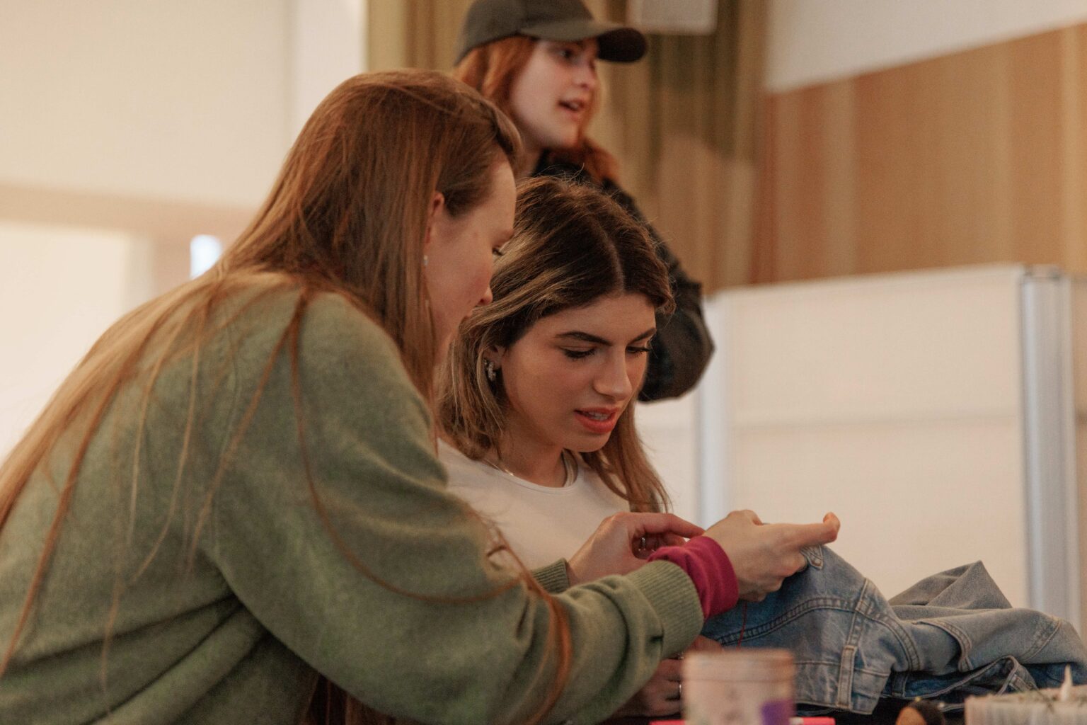 Lisan geeft workshop-deelnemer uitleg over borduren. Ze zit naast de deelnemer en laat zien hoe je het draad door de naald haalt.