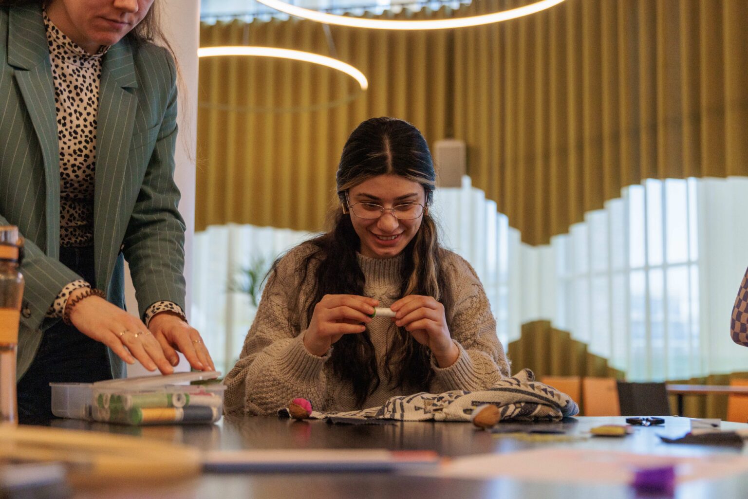 Workshop-deelnemer kijkt met een lach naar beneden naar een klosje witte garen waarmee ze een knoop weer aan haar blouse gaat naaien.