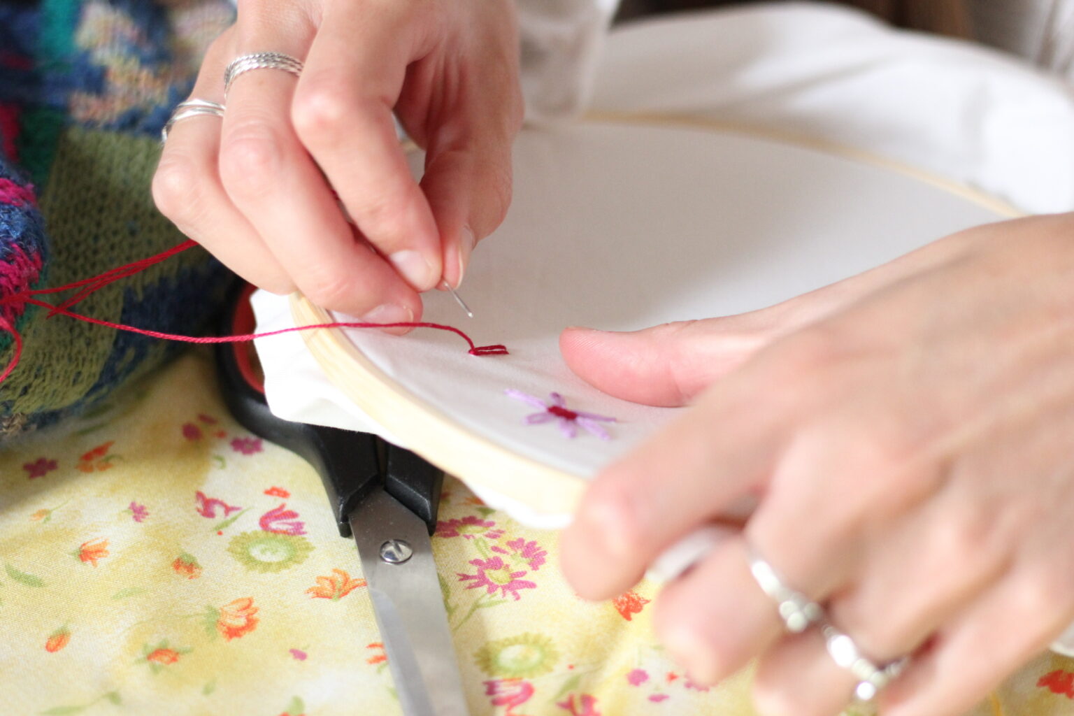 Iemand houdt een borduurring vast waar bloemetjes op geborduurd worden.
